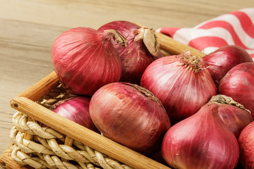 Basket of Red Onions on  wooden background with copy space